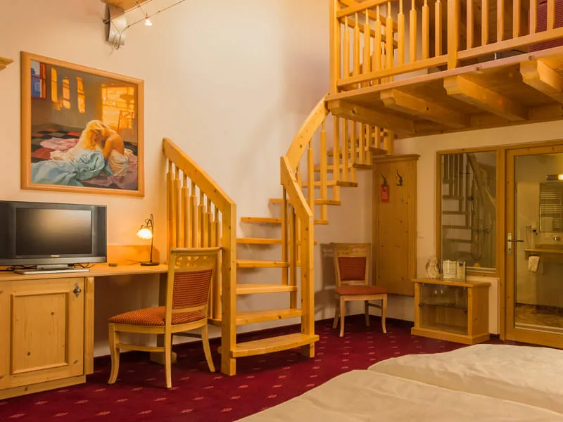 Zimmer mit Doppelbett, Zirbenholz-Treppe zur Galerie und Schreibtischplatz unter der Balkendecke